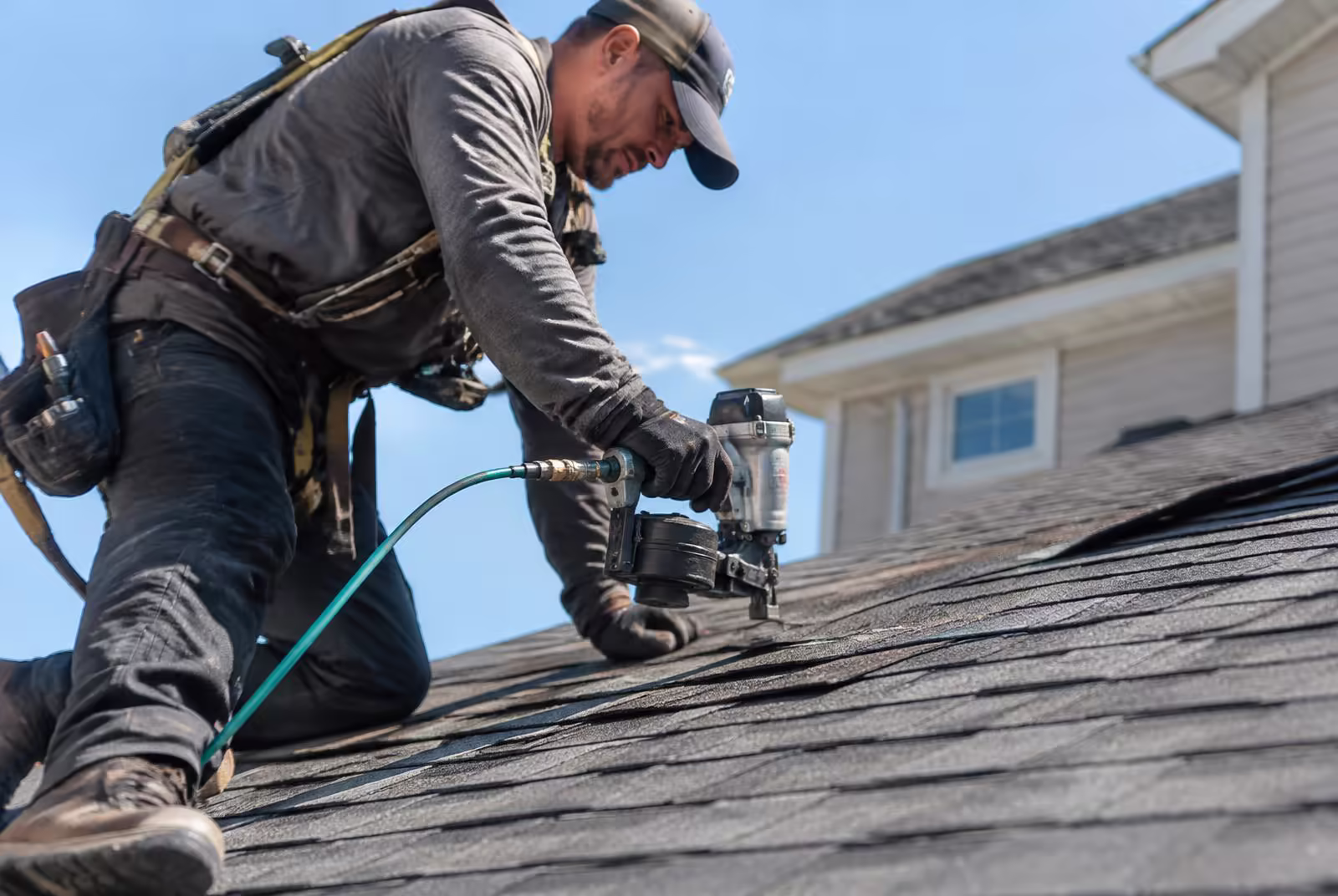 Roofer nailing new asphalt shingles onto a house roof with a nail gun